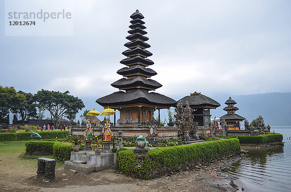 Balinesischer Hindu-Tempel  Ulu Danu Beratan  traditionelle Architektur und hohe Türme mit abgestuften  spitz zulaufenden Dächern in einem Tal am Ufer des Bratan-Sees.