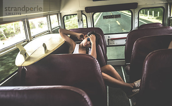 Junge Frau  die mit einem Surfbrett in einem Bus sitzt.