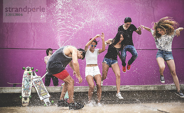 Eine Gruppe junger Leute  die springen  während sie mit Wasser bespritzt werden.