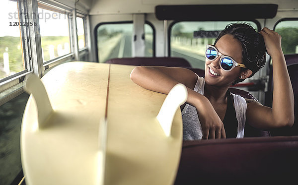 Junge Frau  die mit einem Surfbrett in einem Bus sitzt.