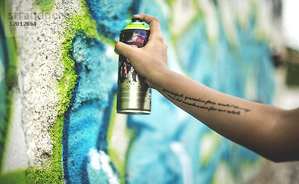 Nahaufnahme einer Person  die ein Graffiti-Tag an eine Wand sprüht.