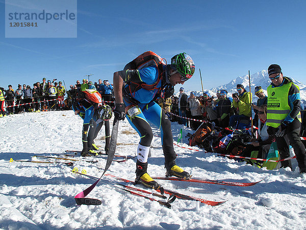 Frankreich  Savoyen  Beaufortain  Areches  während des internationalen Skialpinismus-Rennens der Pierra Menta bereiten 2 Männer mit Helmen und Skianzügen ihre Skier für die Abfahrt vor  umgeben von einer großen Schar von Anhängern