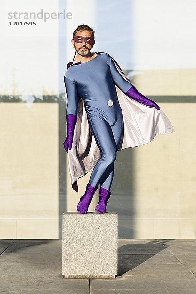 Porträt eines Superhelden  der auf Beton an einer Glaswand steht.