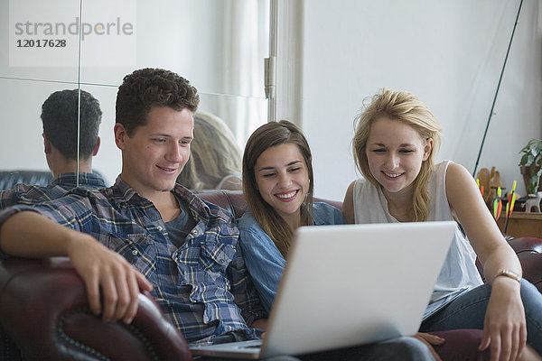 Lächelnde junge Freunde beim Sitzen auf dem Sofa zu Hause mit dem Laptop