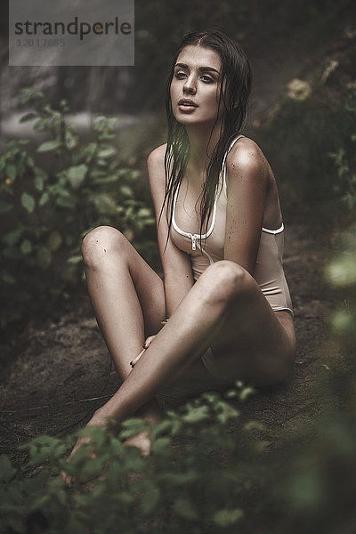 Nachdenklich sinnliche junge Frau in Badebekleidung im Wald sitzend