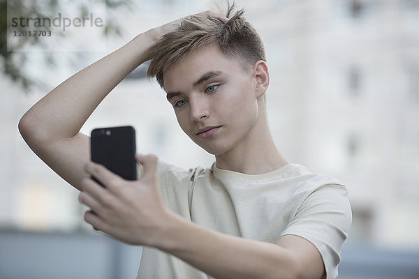 Teenager Junge nimmt Selfie vom Handy mit Hand in Haar