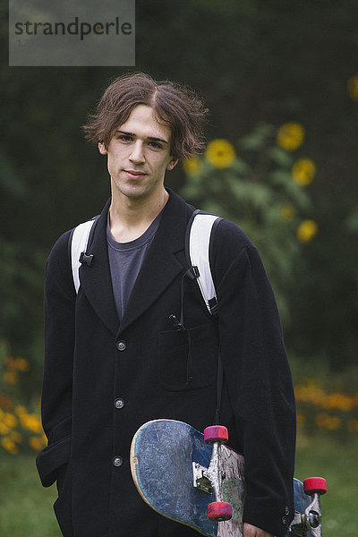 Porträt eines selbstbewussten jungen Mannes mit Skateboard beim Stehen im Park