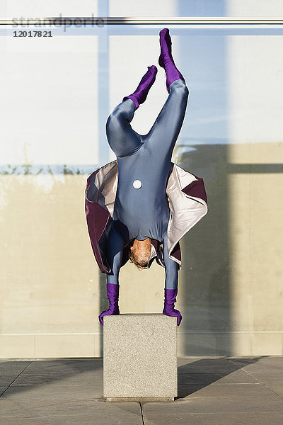 Superheld macht Handstand auf Beton gegen Glaswand