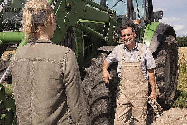 Männlicher Bauer im Gespräch mit einer Frau  während er an einem sonnigen Tag an einer Landmaschine steht.