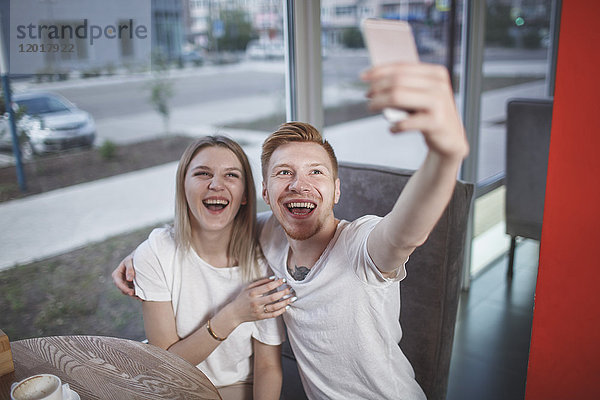 Großer Blickwinkel auf ein glückliches junges Paar  das im Restaurant sitzt und sich selbst mit dem Handy fotografiert.