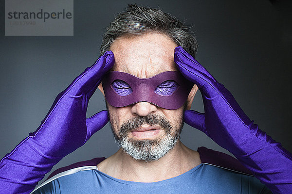 Nahaufnahme eines Superhelden mit Kopfschmerzen vor grauem Hintergrund