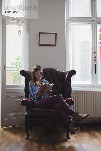 Schöne junge Studentin sitzt auf einem Sessel und liest zu Hause ein Buch.