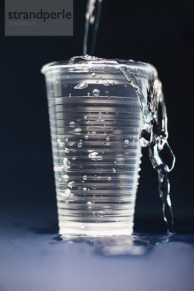 Nahaufnahme von Wasser  das in überlaufendes Glas auf dem Tisch vor schwarzem Hintergrund strömt.