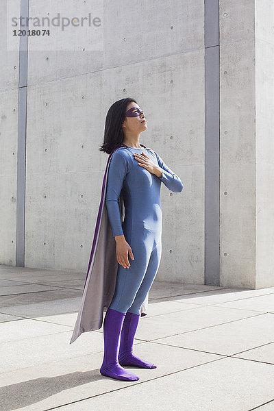 Selbstbewusste Frau im Superheldenkostüm auf dem Boden an der Wand stehend