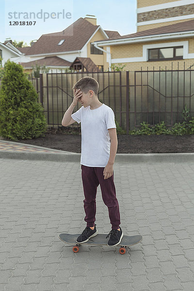 Junge auf Skateboard auf Fußweg gegen Häuser