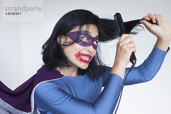 Frau als Superheldin verkleidet  die das Haar vor grauem Hintergrund glättet.