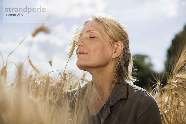 Nachdenklich lächelnde Frau mit geschlossenen Augen  die sich an einem sonnigen Tag inmitten von Getreide auf dem Bauernhof ausruht.