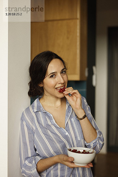 Porträt einer jungen Frau  die zu Hause rote Johannisbeeren isst.