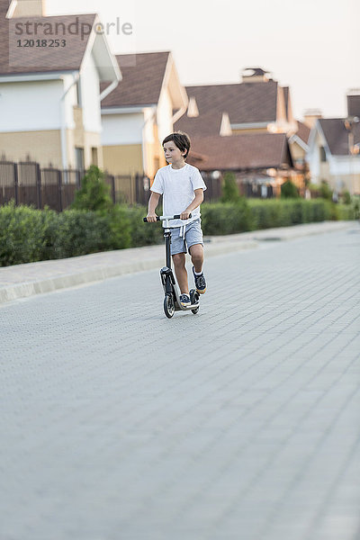 Junge fährt Roller auf gepflasterter Straße in der Stadt