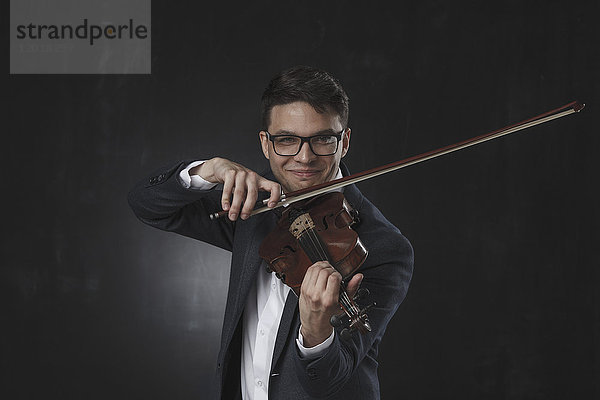 Selbstbewusst lächelnder junger Mann beim Geigenspiel vor schwarzem Hintergrund