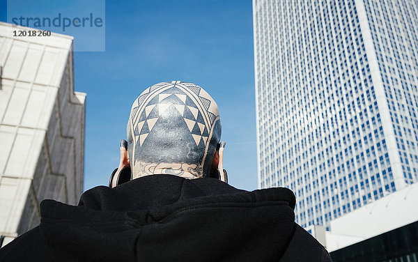 Flachwinkel-Rückansicht des Mannes mit Tattoos und Ohrstöpseln gegen Wolkenkratzer in der Stadt