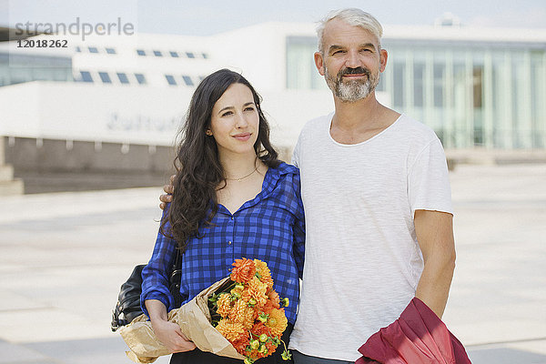 Zuversichtliches Paar mit Blumenstrauß in der Stadt an einem sonnigen Tag