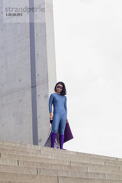 Niedriger Blickwinkel des selbstbewussten weiblichen Superhelden  der auf Stufen gegen den klaren Himmel steht.