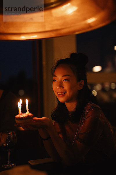 Glückliche Frau hält kleine Geburtstagstorte mit Kerzen in der Dunkelkammer