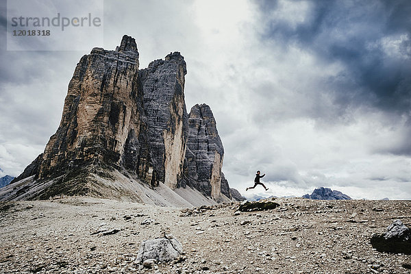 Tiefblick auf einen Teenager  der über Felsen in den Alpen gegen den bewölkten Himmel springt  Südtirol  Italien
