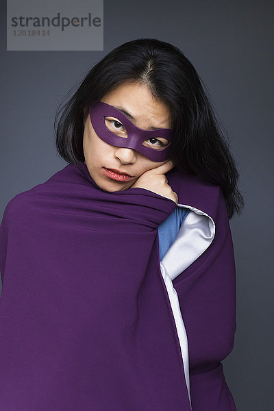 Porträt einer Superheldin mit violettem Umhang auf grauem Hintergrund