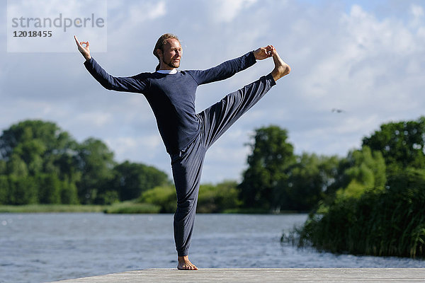 Reifer Mann beim Yoga am Pier am See gegen den Himmel