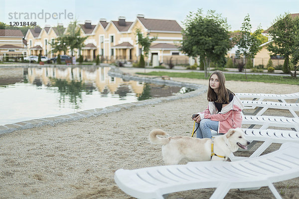 Porträt eines jungen Mädchens auf einem Liegestuhl von einem Hund am Strand.