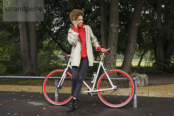 Mittlere erwachsene Frau beim Telefonieren mit dem Fahrrad im Park