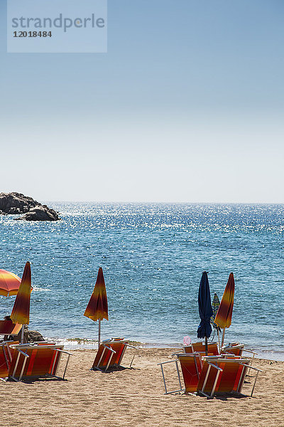 Geschlossene Sonnenschirme mit Liegestühlen am Strand gegen klaren blauen Himmel an sonnigen Tagen