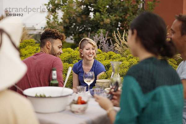 Glückliche männliche und weibliche Freunde sitzen am Außentisch auf der Terrasse.