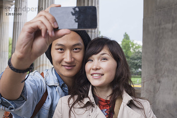 Lächelnder Mann nimmt Selfie mit junger weiblicher Freundin mit