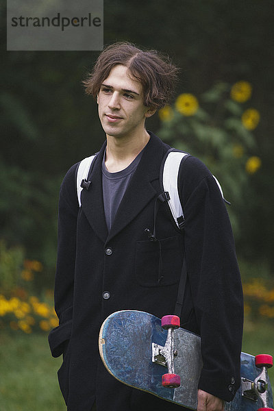 Nachdenklicher junger Mann mit Skateboard beim Stehen im Park