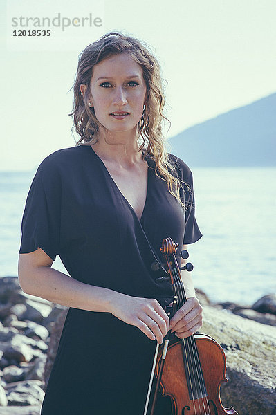 Porträt einer schönen Frau  die am Seeufer steht und Geige hält