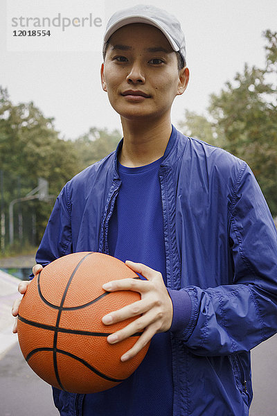 Porträt eines jungen Mannes  der den Ball hält  während er im Park steht.