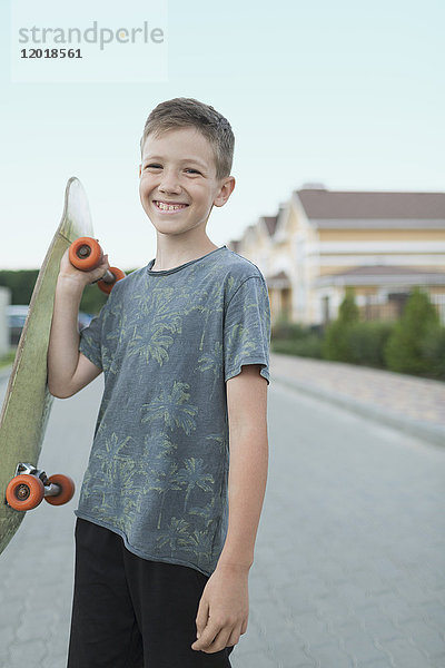 Porträt eines lächelnden Jungen mit Skateboard im Stehen auf der Straße