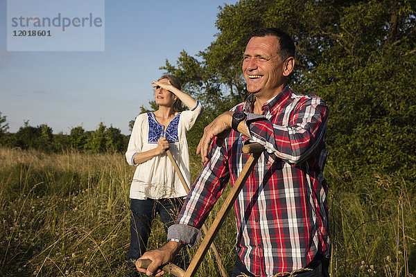 Lächelndes reifes Paar mit Ausrüstung  das an einem sonnigen Tag auf dem Bauernhof steht.