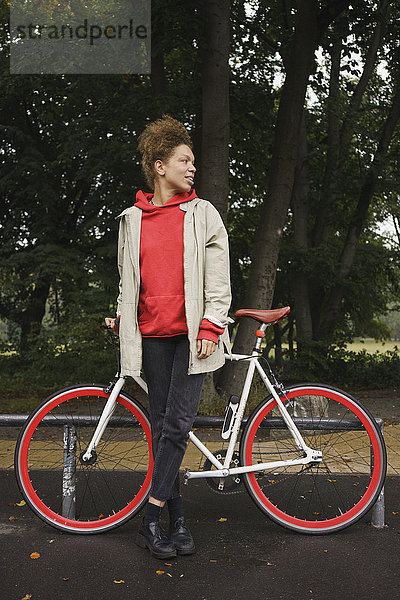 Mittlere erwachsene Frau steht mit dem Fahrrad im Park