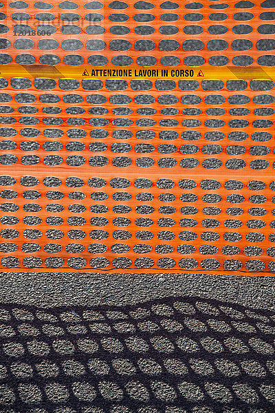 Hochwinkelansicht des orangefarbenen Zauns mit Schatten auf der Straße