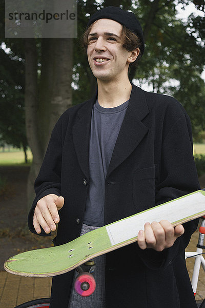 Fröhlicher junger Mann mit Skateboard im Park