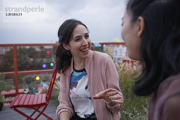 Fröhliche Frau im Gespräch mit einer Freundin auf der Terrasse