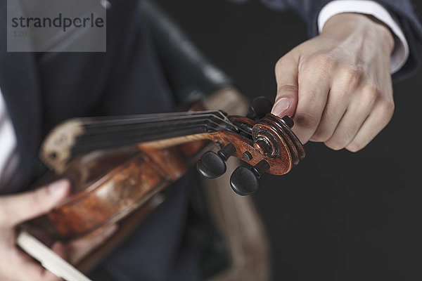 Abgeschnittenes Bild eines Musikers beim Stimmen von Geigensaiten