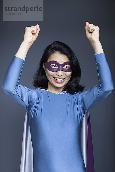 Porträt einer aufgeregten weiblichen Superheldin mit erhobenen Armen auf grauem Hintergrund
