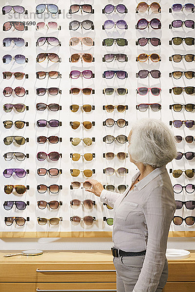 Seitenansicht der Seniorin bei der Wahl der Sonnenbrille im Geschäft