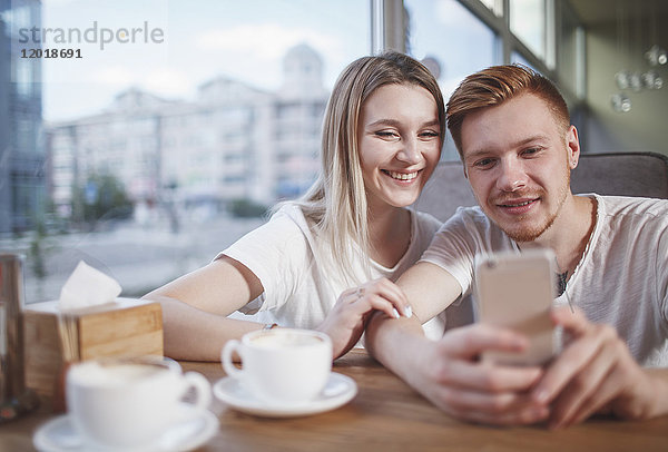 Fröhliches junges Paar beim Sitzen im Restaurant per Handy