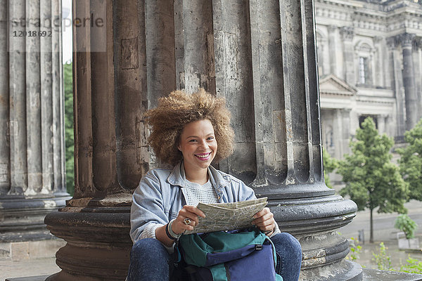 Porträt einer lächelnden jungen Afro-Touristin sitzend mit Karte an der Säule im Alten Museum